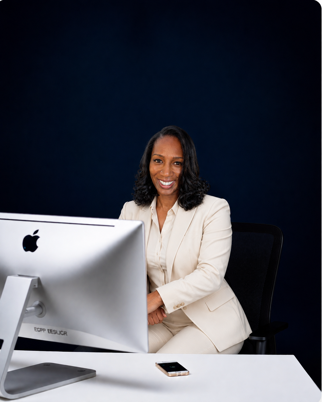 Professional in a cream business suit smiling at a desk workstation